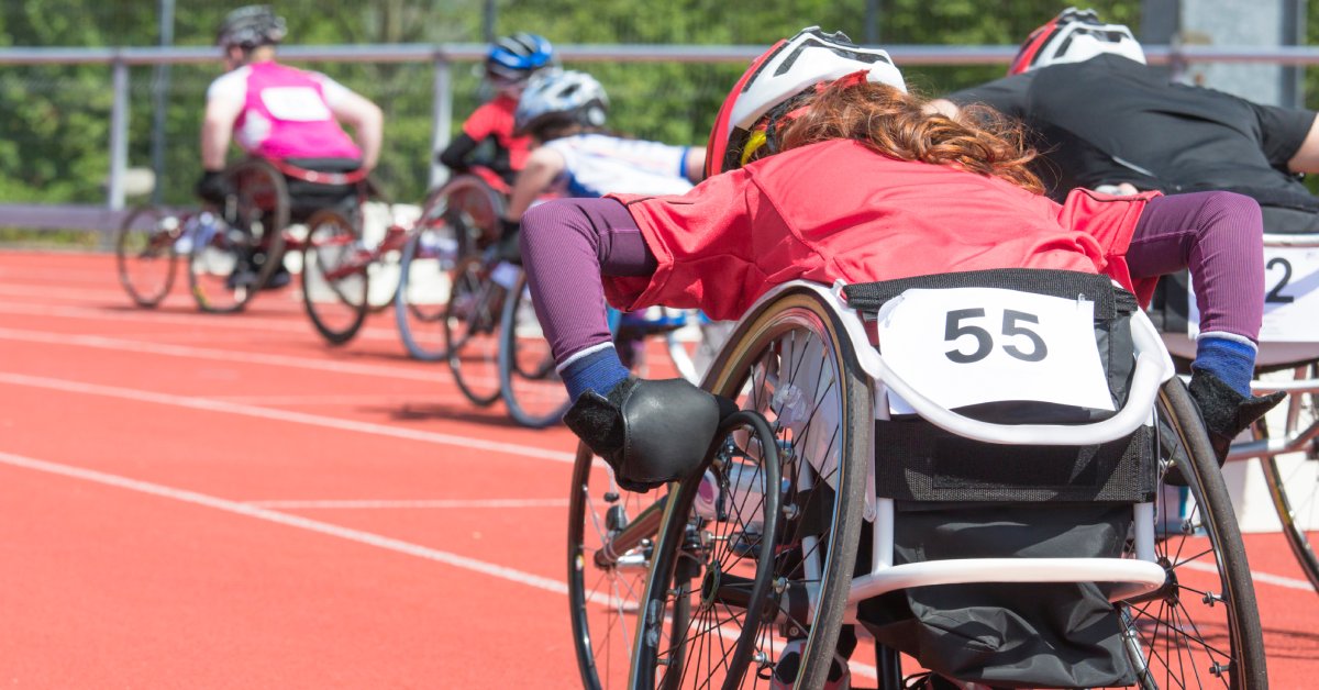 A close-up of a woman in a performance wheelchair with a paper sign reading 